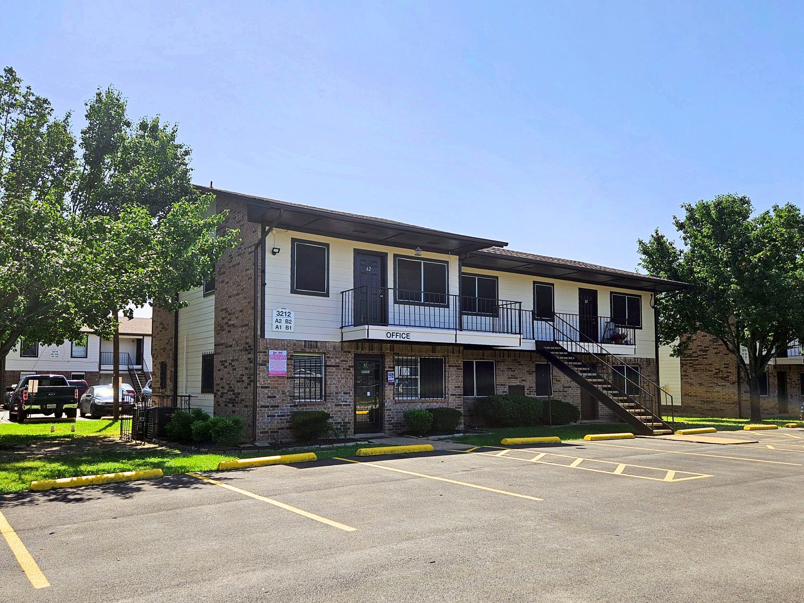 Two-story brick and siding apartment building with ground-floor office entrance, exterior stairs and parking lot