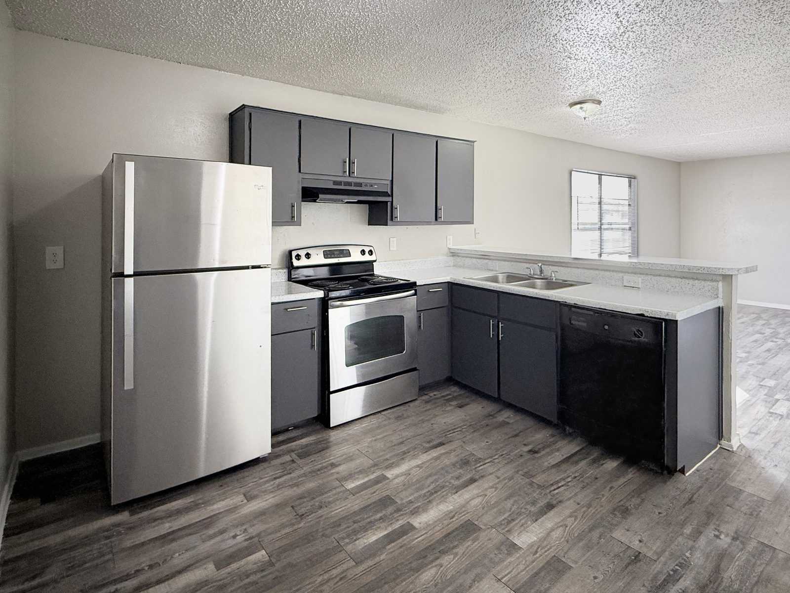 Kitchen with dark grey cabinets, stainless refrigerator and range, dishwasher, sink and window