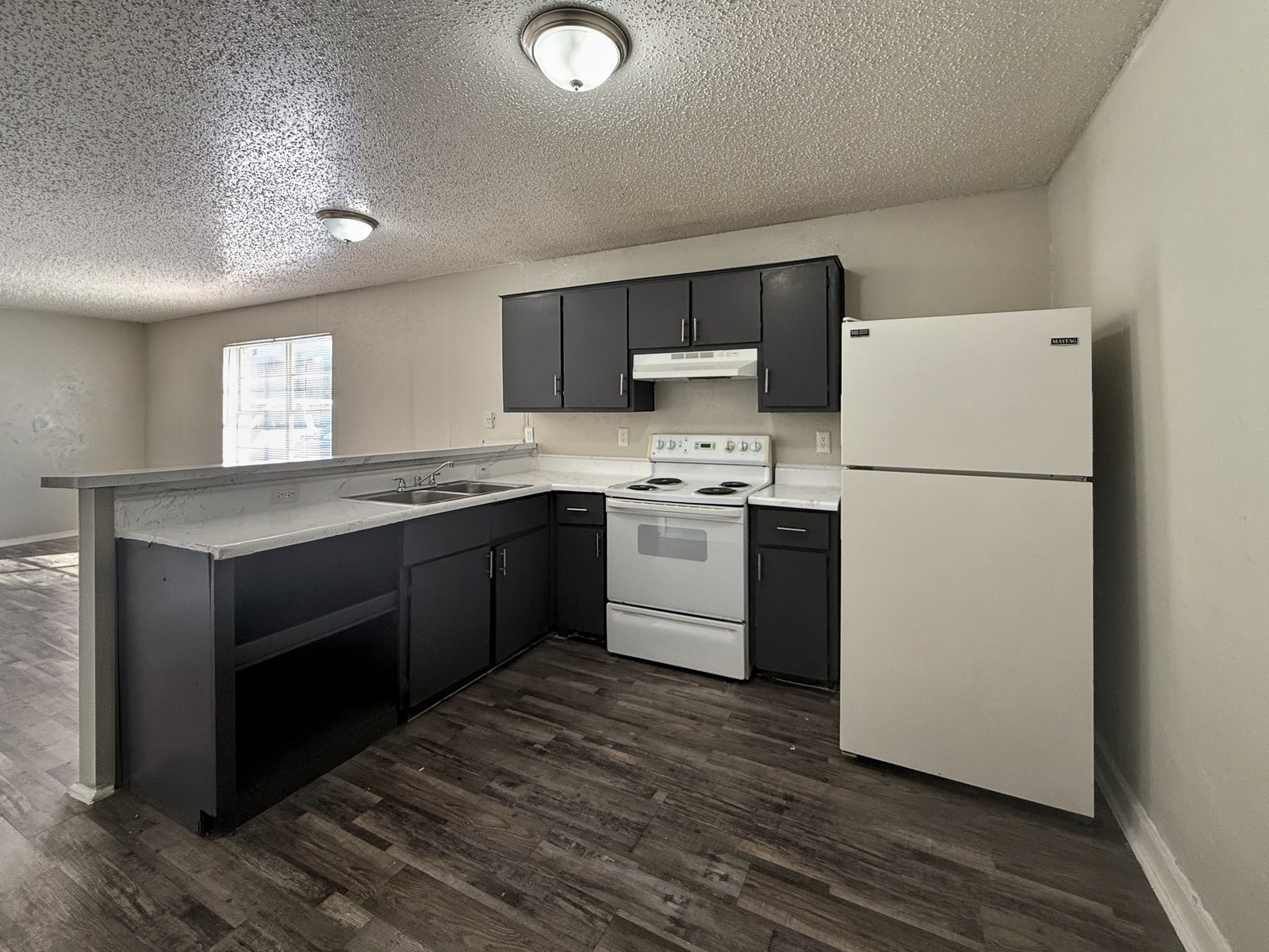 Kitchen with dark cabinets, white range and refrigerator, breakfast bar and living room window beyond