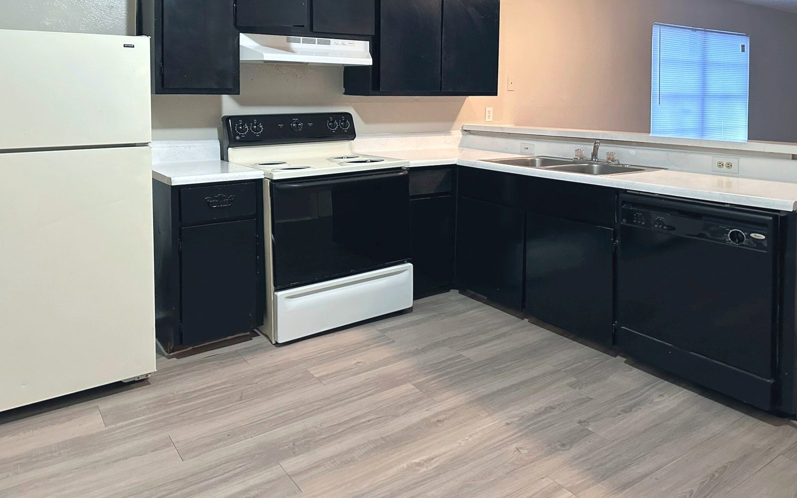 L-shaped kitchen with black cabinets, a white range and refrigerator, and a dishwasher