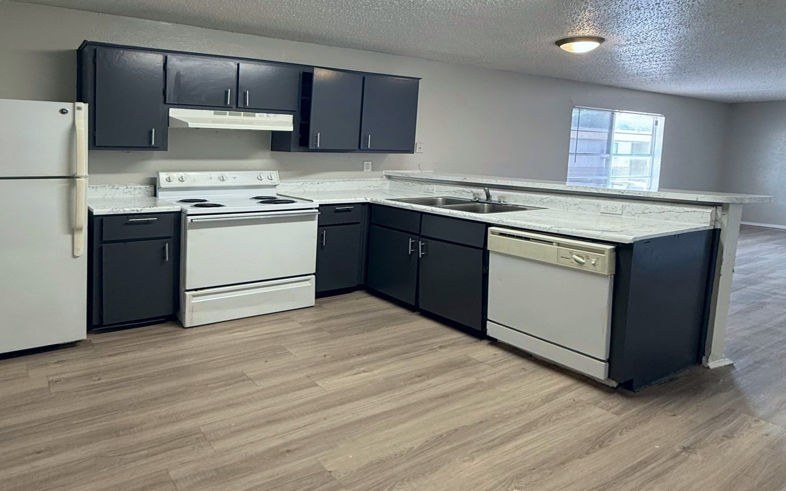 Open L-shaped kitchen with gray cabinets, white appliances and a long counter