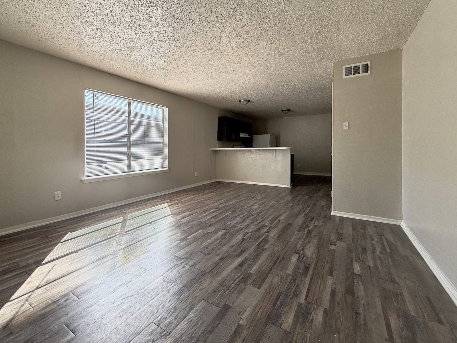 Living room with window, wood-look floor and view through to the kitchen breakfast bar