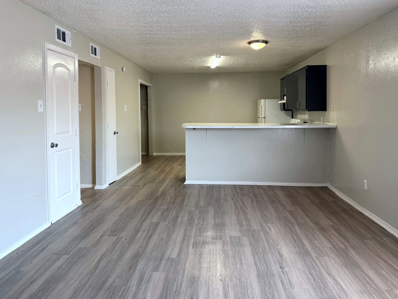 Empty living room with gray vinyl plank floor, white doors and a kitchen breakfast bar counter