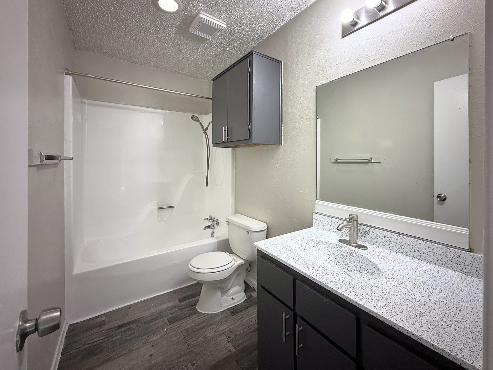 Bathroom with tub and shower, toilet, granite vanity with dark cabinets and large mirror